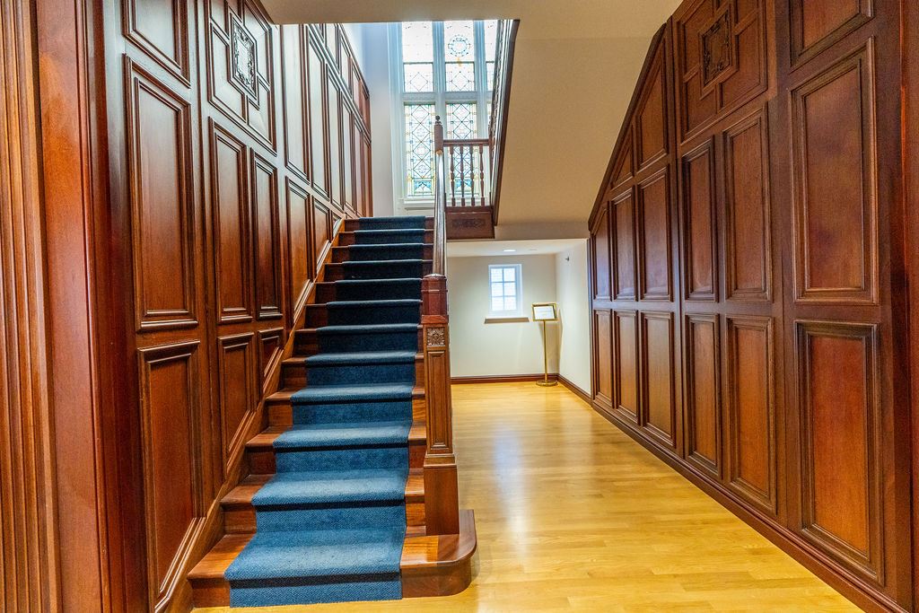 A staircase with wooden rails and blue carpet, and a window