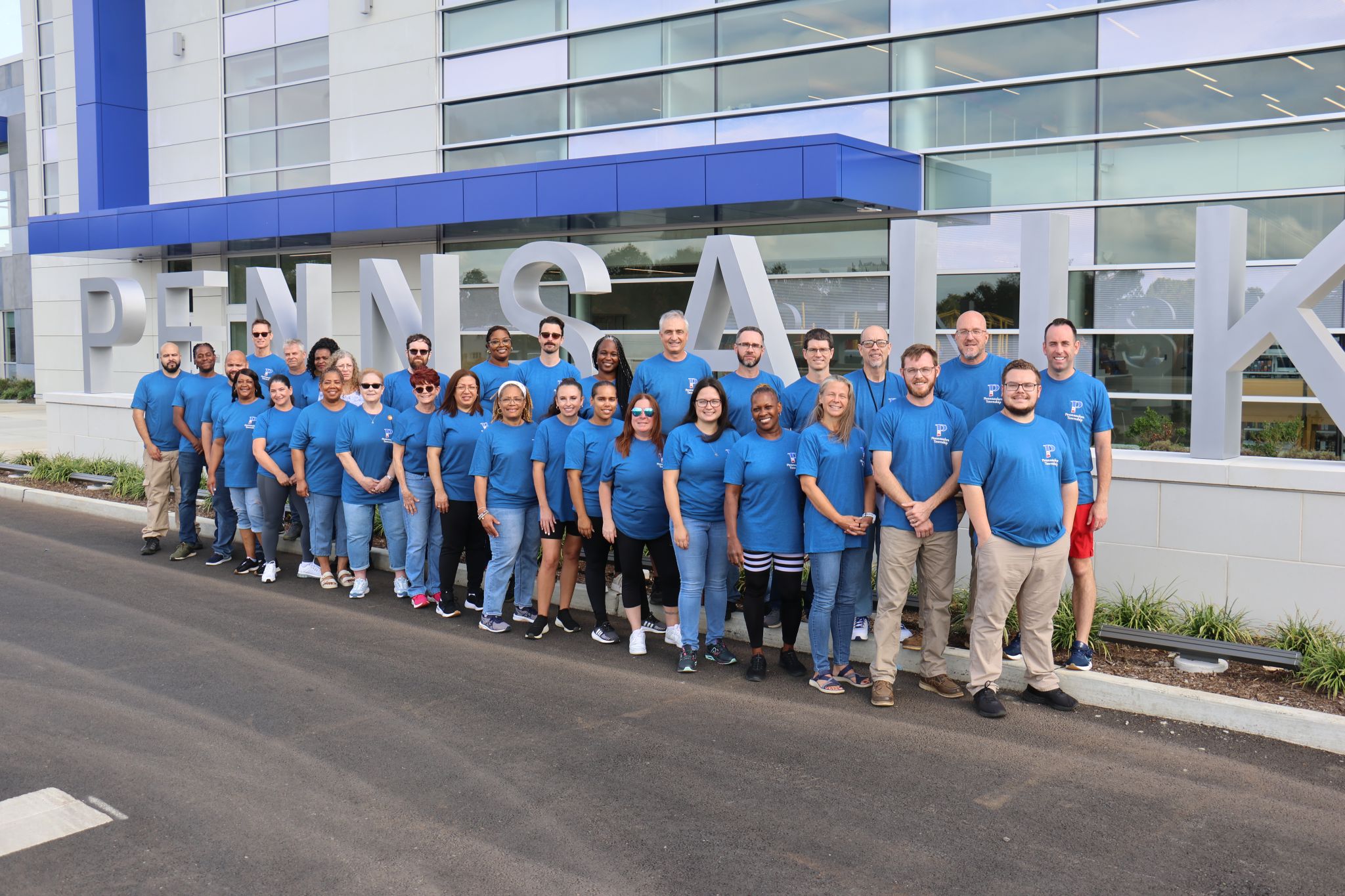 Large group of men and women in blue t-shirts standing in front of Pennsauken building sign