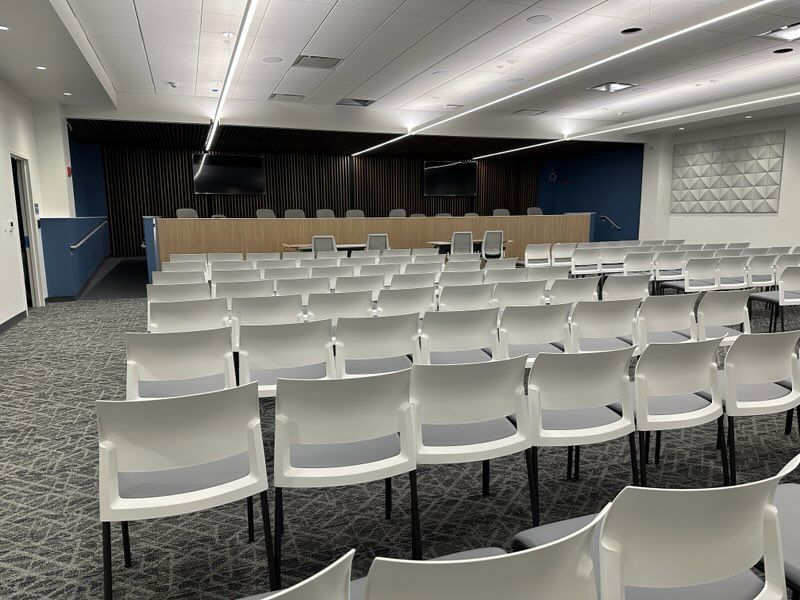 Meeting room with white chairs for audience and a facing dias with chairs.